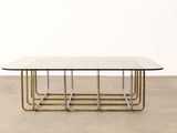 a glass and brass coffee table on a concrete floor
