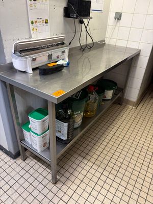 table de travail en acier inoxydable dans une cuisine professionnelle, sur laquelle sont posés des seaux contenant des produits d'entretien