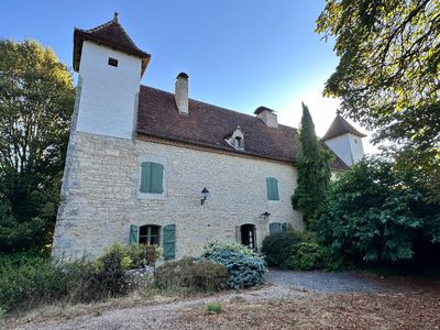 an old stone building with green shutters in the middle of a wooded area