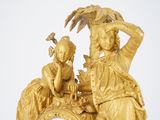 a gold clock with a woman and a child sitting on it