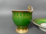 a green and gold cup and saucer sitting on a table