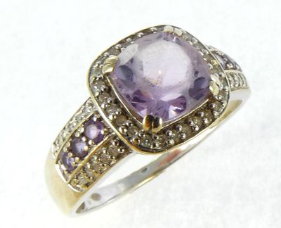 a close up of a ring with a purple stone surrounded by diamonds
