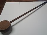 a long wooden stick on a white surface next to a wooden spoon