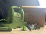 un petit aspirateur vert posé sur une table, à côté d'une boîte