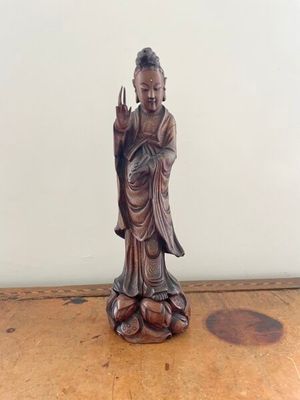 statue of a person sitting on a wooden table with a white wall in the background