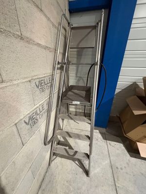 une échelle métallique appuyée contre un mur, à côté d'un carton