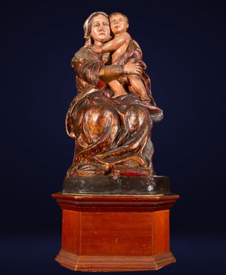 une statue ancienne représentant une femme tenant un enfant dans ses bras, posée sur un socle en bois