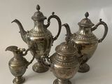 three silver teapots and two silver spoons on a table