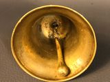 an antique brass bell with a wooden handle on a brown surface