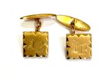 two gold cufflinks with initials on them on a white surface
