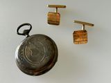 a silver pocket watch and a pair of cufflinks on a table
