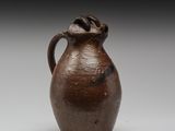 une image représentant un vase marron muni d'une anse, posé sur une surface blanche