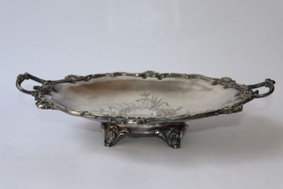 un plat ancien en argent avec des poignées, posé sur un socle, sur une surface blanche
