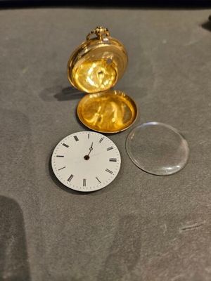 une montre de poche en or posée sur une table, à côté d'une loupe