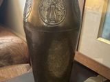 un vase ancien en laiton posé sur une table, à côté d'une photo encadrée