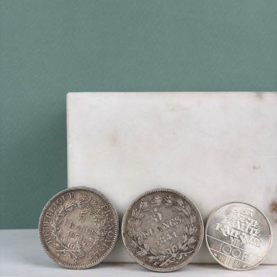 Trois pièces de monnaie sont posées sur une dalle de marbre, près d'un mur vert.