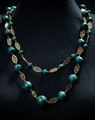 un collier composé de perles vertes et de feuilles dorées, présenté sur un mannequin