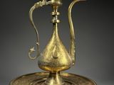 une théière ancienne en laiton posée sur une soucoupe, munie d'une anse