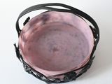a pink bowl sitting on a white surface with a black handle