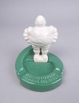 une figurine blanche représentant un homme posée sur un cendrier vert