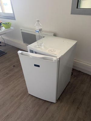 un petit réfrigérateur blanc dans le coin d'une pièce