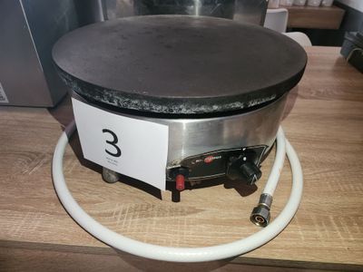 une machine à crêpes noire et argentée posée sur une table en bois