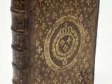 an old book with a gold and black cover on a white surface