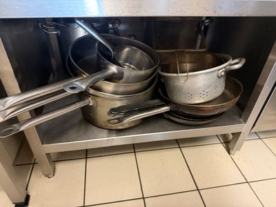 Des casseroles et des poêles sont posées sur une étagère en acier inoxydable dans une cuisine