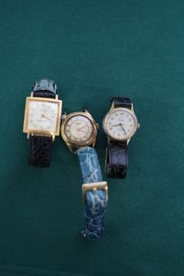 Trois montres sont posées sur un tissu vert, sur fond vert.