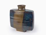 un vase brun et bleu posé sur une surface blanche