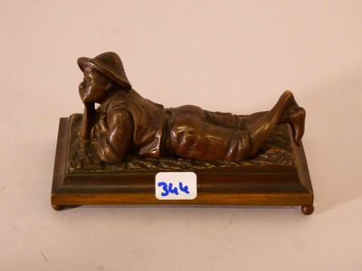 figurine en bronze représentant un homme allongé sur un banc, coiffé d'un chapeau