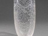 un vase en verre gravé posé sur une table près d'un mur gris