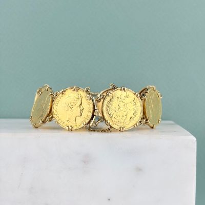 un gros plan d'un bracelet composé de pièces d'or posé sur un bloc de marbre