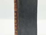 an old book with a black cover sitting on top of a white surface