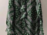une chemise à motifs cachemire verts et blancs suspendue à un cintre devant un mur blanc