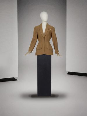 mannequin vêtu d'une veste marron et d'une jupe noire dans une pièce blanche
