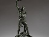 une statue en bronze représentant un homme tenant une batte de baseball, posée sur un socle en bois