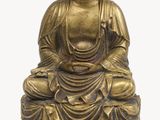 a gold statue of a buddha sitting on a white surface