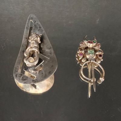deux bagues en argent et une broche en argent posées sur un fond noir