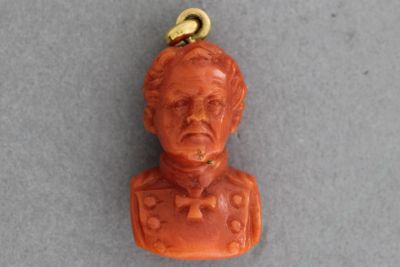 une image représentant un buste sculpté rouge d'un homme, suspendu à une chaîne plaquée or
