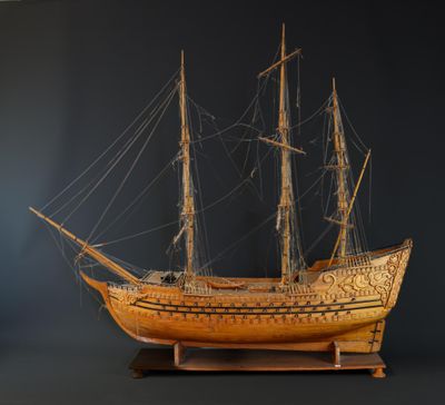 une maquette de bateau en bois posée sur un socle, sur fond noir