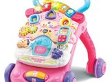 un trotteur rose pour bébé, surmonté de jouets, posé sur une surface blanche
