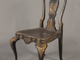 une chaise ancienne noire et dorée sur fond gris