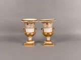 paire de vases dorés et blancs munis d'anses et posés sur des socles