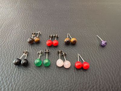 six pairs of earrings are arranged on a black surface