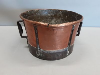 une vieille casserole en cuivre posée sur une table blanche