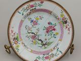 une image représentant une assiette décorée de fleurs et d'oiseaux, posée sur un support