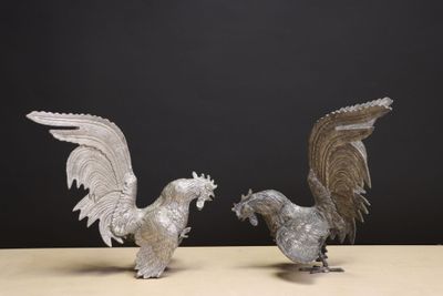 pair of silver metal rooster figurines on table against black background