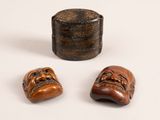 deux petits masques en bois et une boîte en bois posés sur une surface blanche