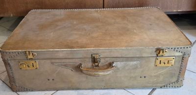 une vieille valise posée par terre à côté d'un meuble